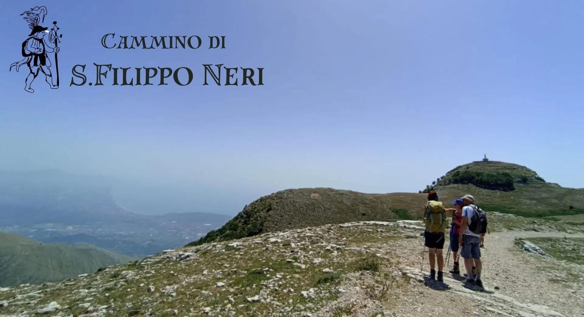 Tre escursionisti con zaino, visti di spalle, camminano su un sentiero di cresta con un'ampia vista sulla vallata e sulla cima in lontananza