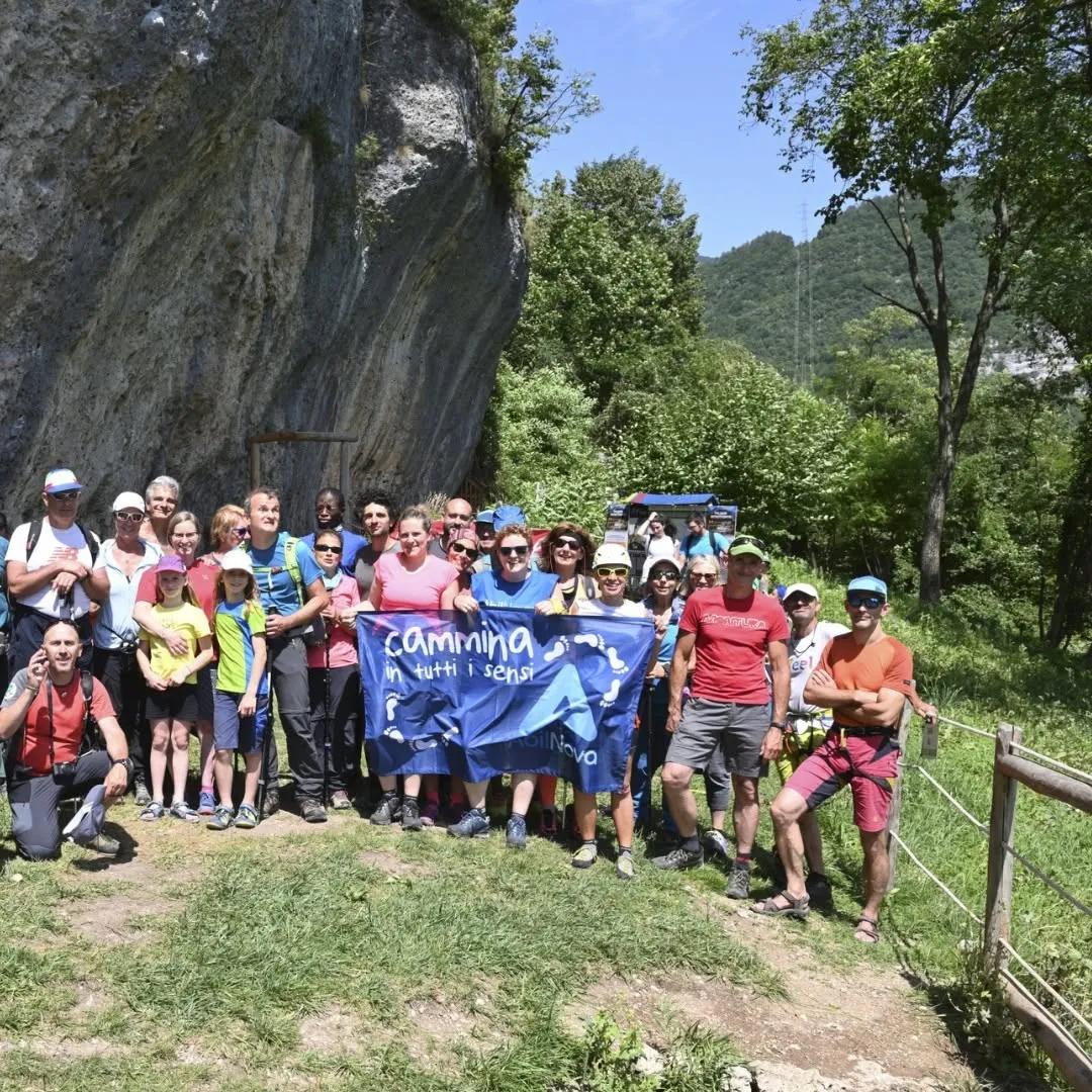 Gruppo di camminatori in posa davanti a una parete rocciosa e al bosco, con uno striscione blu del Cammino San Vili