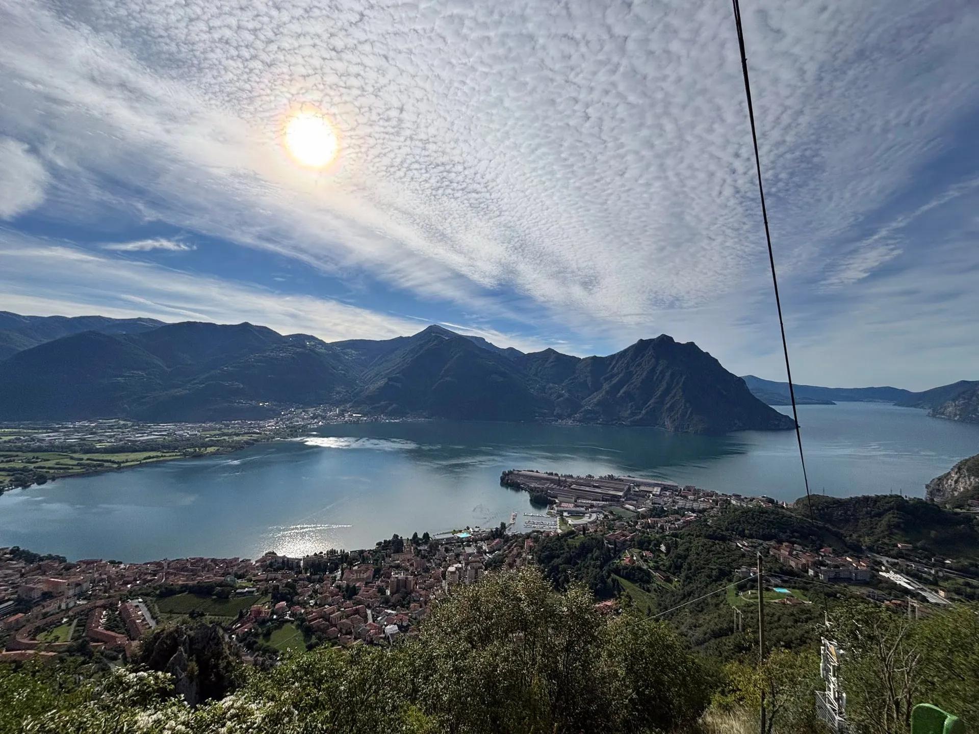 Veduta dall’alto del Lago d’Iseo con un borgo sulla riva e le montagne sullo sfondo, lungo il Cammino dei Tre Laghi